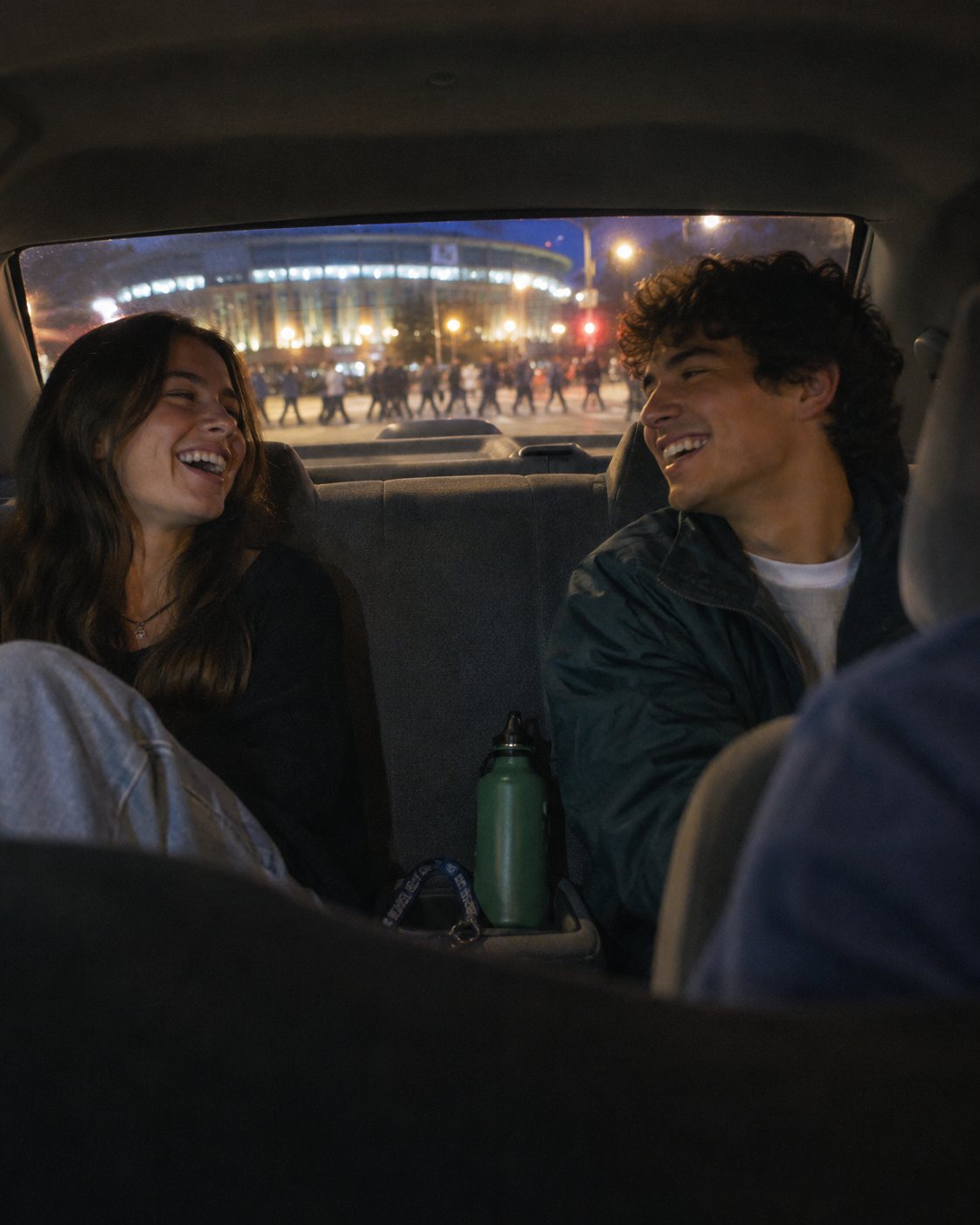 Two students laughing in the back seat of a car at night.
